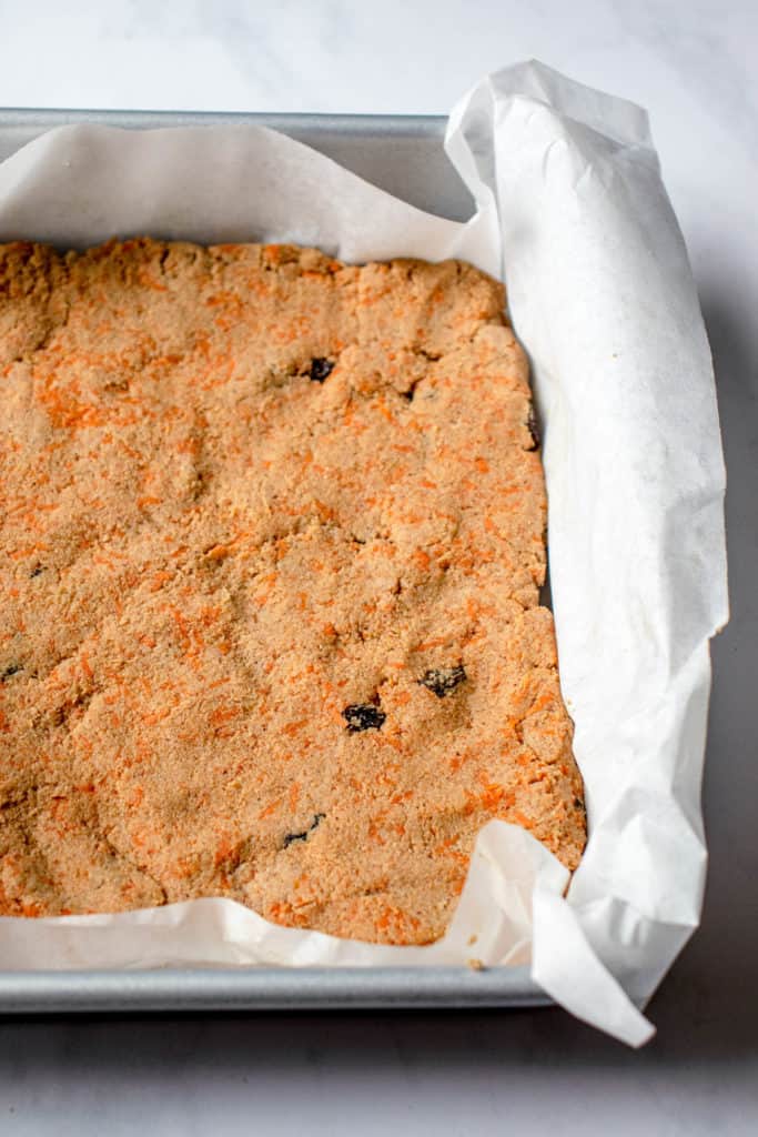 paleo carrot cake pressed into a parchment lined sheet pan before being placed into the oven 