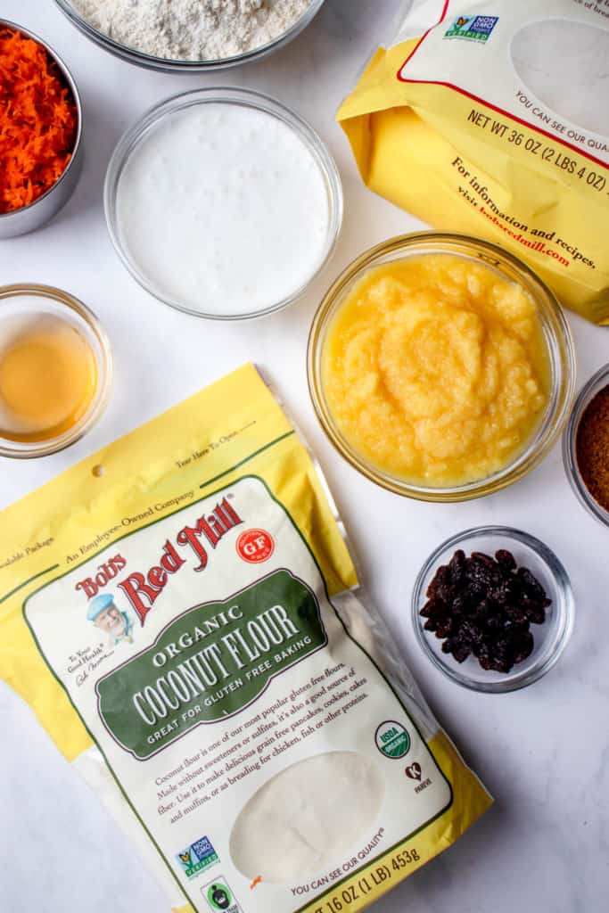overhead shot of clear glass bowls with carrot cakes ingredients. There are two yellow, white and red Bob's Red Mills bags of flour in the frame - one of organic coconut flour and the other of cassava flour