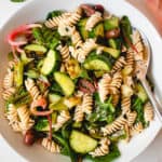 overhead shot of a white plate with paleo pasta salad consisting of grain-free pasta, spinach, olives, cucumbers, green onions and pickled red onions.