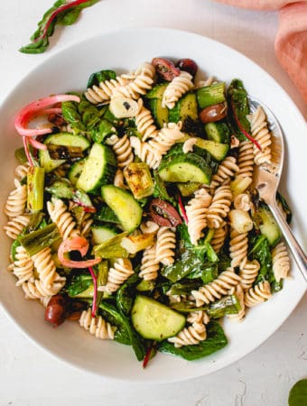 overhead shot of a white plate with paleo pasta salad consisting of grain-free pasta, spinach, olives, cucumbers, green onions and pickled red onions.