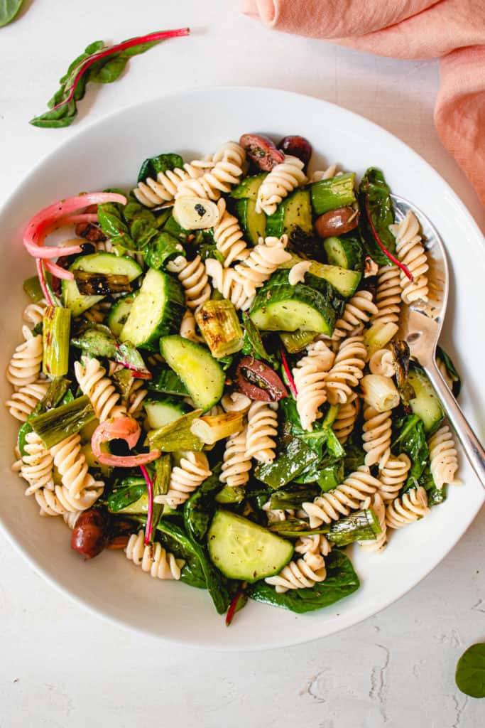 overhead shot of a white plate with paleo pasta salad consisting of grain-free pasta, spinach, olives, cucumbers, green onions and pickled onions.