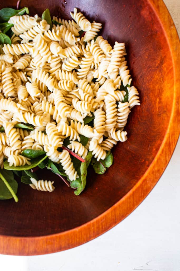 overhead shot of a wooden bowl with fusilli cassava pasta and spinach