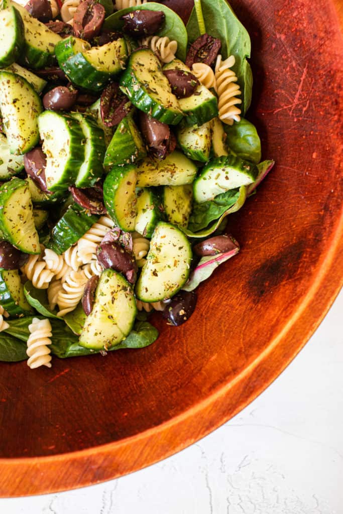 wooden bowl with herbed cucumbers, olives, spinach and cassava pasta