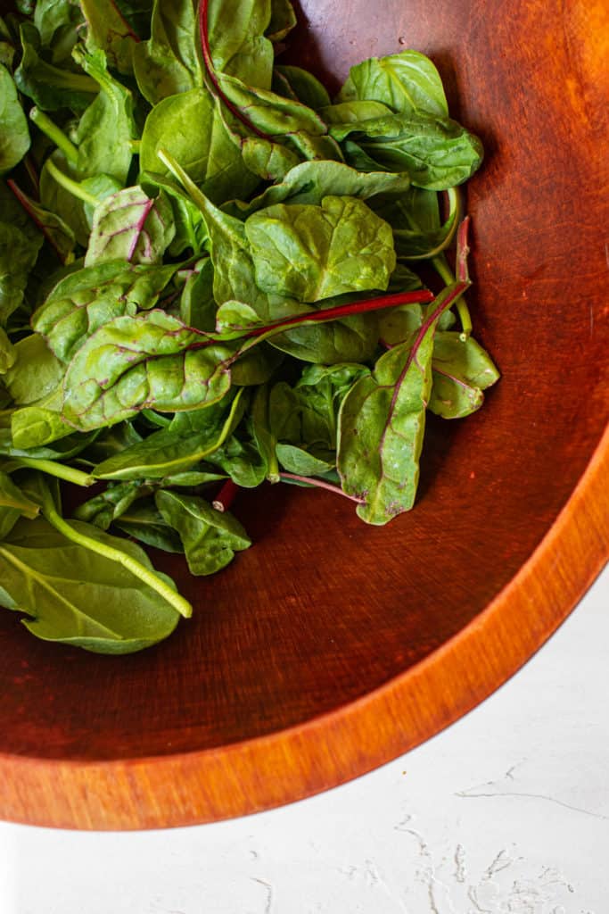 close up shot of a wooden bowl with spinach leaves