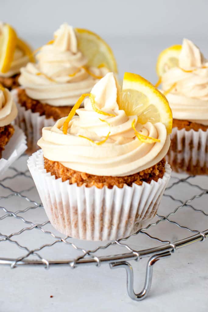 close up shot of a lined, lemon garnished cupcake with several cupcakes in the background.
