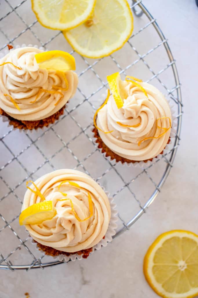 Overhead shot of three lemon olive oil cupcakes with lemon vanilla frosting on a cooling rack