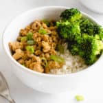 two white bowls with gluten free orange chicken, cauliflower rice and steamed broccoli