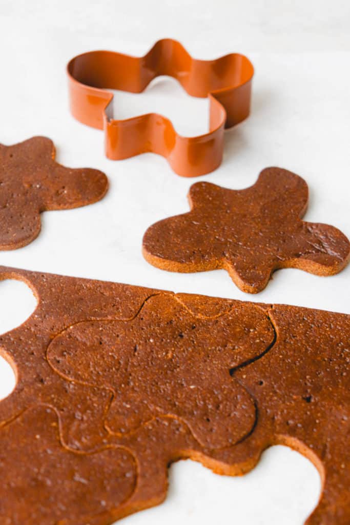 gingerbread cookie dough with a gingerbread person cookie cutter, and with cut outs of the dough on a white countertop.