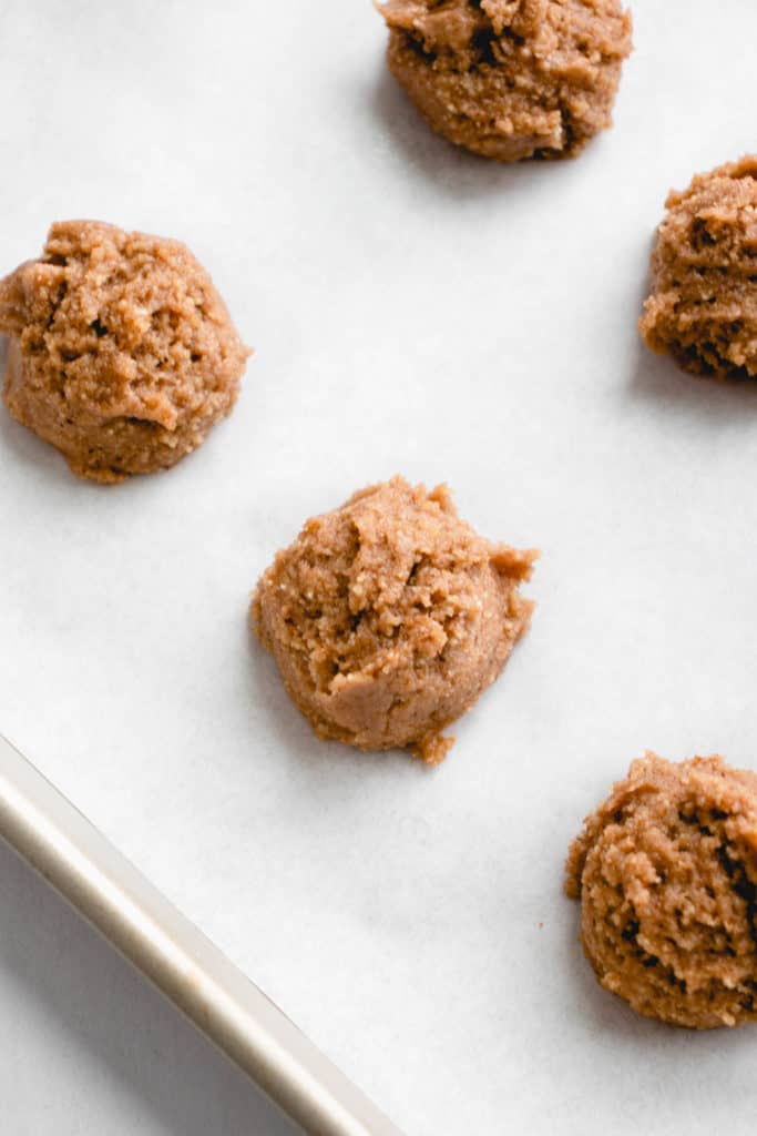 stainless steel sheet pan lined with a white piece of parchment paper and six balls of pre-cooked gingersnap cookie dough