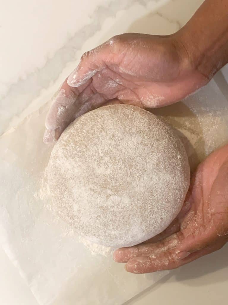 brown hands transferring proofed boule to parchment paper