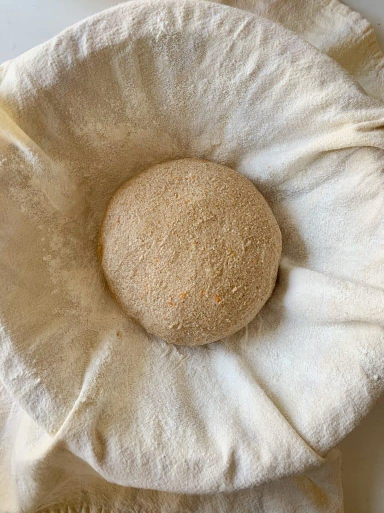 round shaped and smoothed dough in a towel-lined and floured bowl