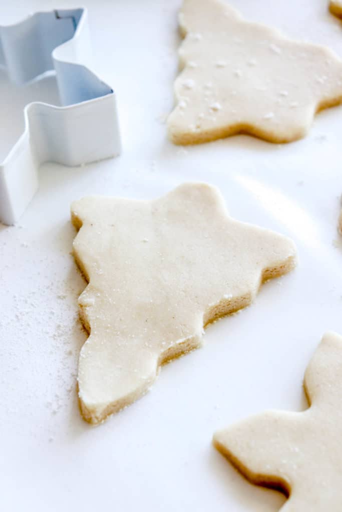 cut out christmas tree cookies with a snowflake cookie cutter on a white parchment paper sheet