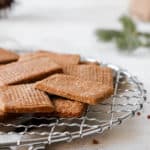 gluten free spiced shortbread cookies on a metal round cooling rack against a grey backdrop with a beige cloth napkin and a jar of cookies blurred in the background