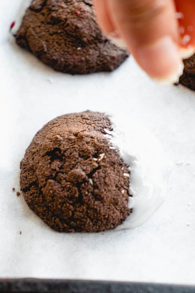 hand sprinkling shredded coconut on chocolate cookie that is half dipped in coconut butter