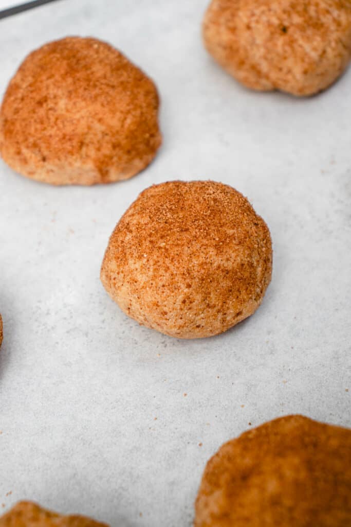 Balls of snickerdoodle cookie dough rolled in cinnamon-sugar and placed on a parchment-lined baking sheet