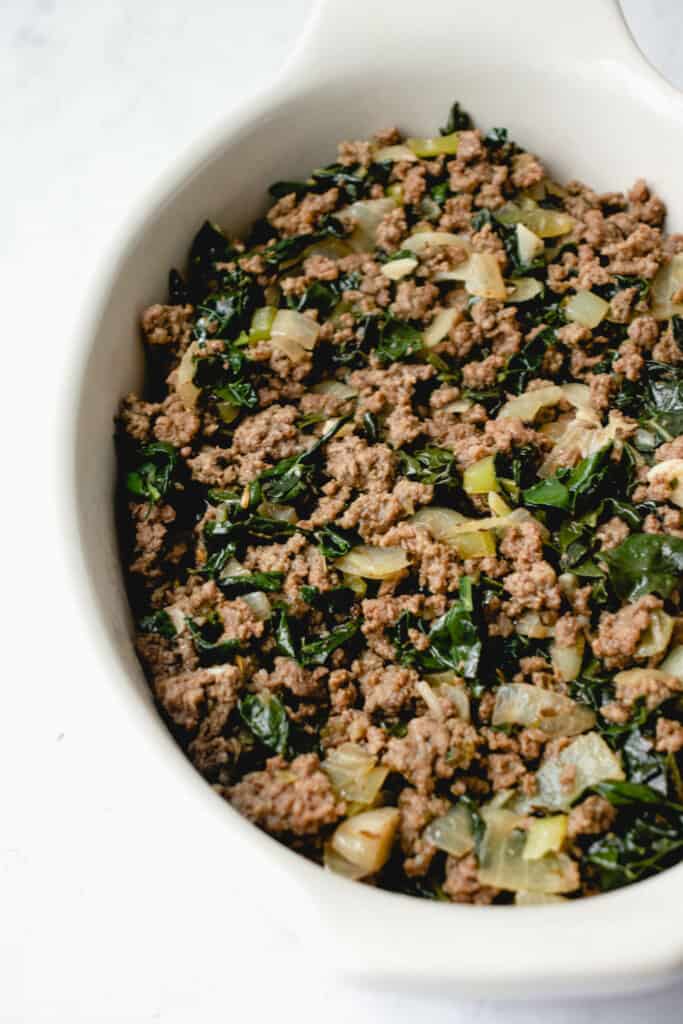 Oval cream casserole dish with ground beef, sautéed onions, celery and kale