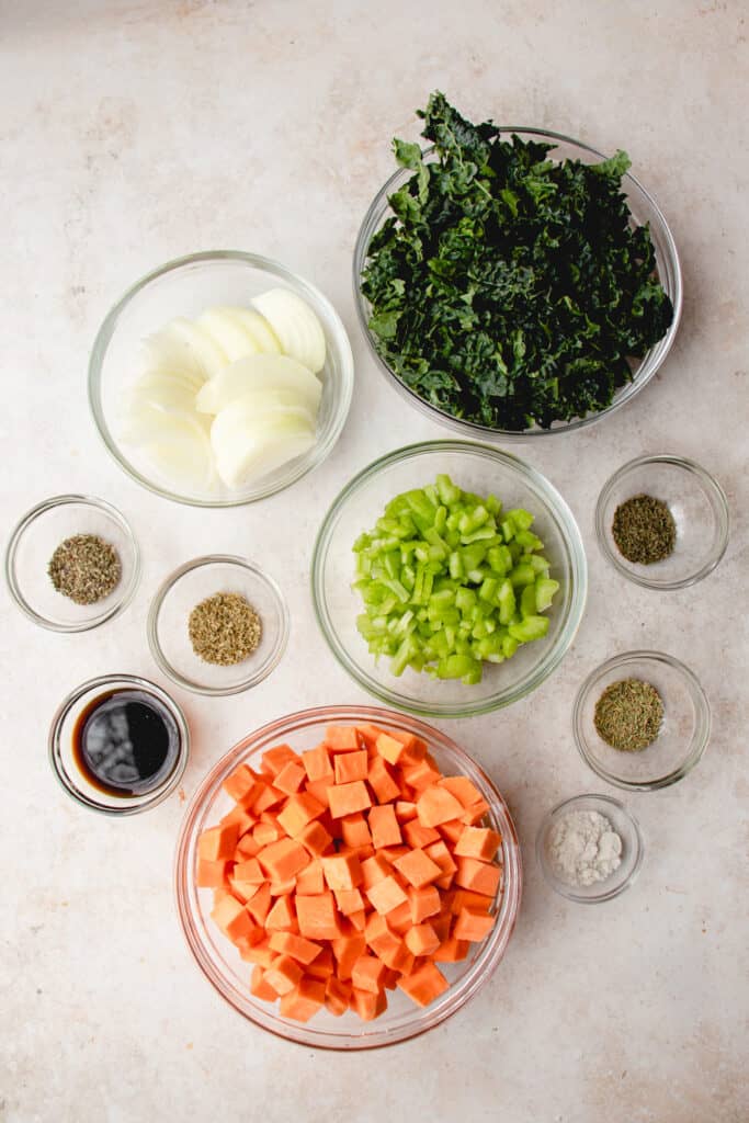 overhead shot of glass bowls with the ingredients for the beef and kale casserole including cubed orange sweet potatoes, dried herbs, diced celery and onions and coconut aminos