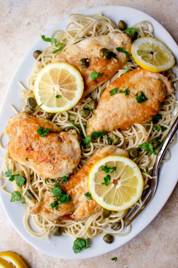 Chicken Piccata on a bed of grain-free pasta on a serving dish, garnished with lemons and parsley.