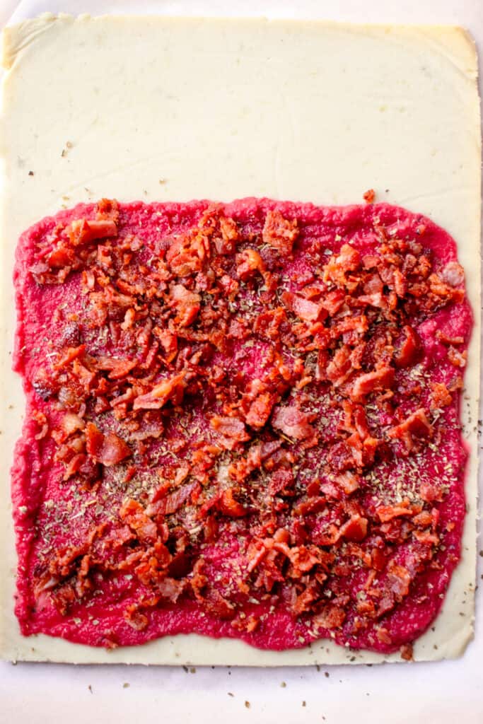 rectangular pizza dough with lower third spread with tomato sauce, herbs and bacon 