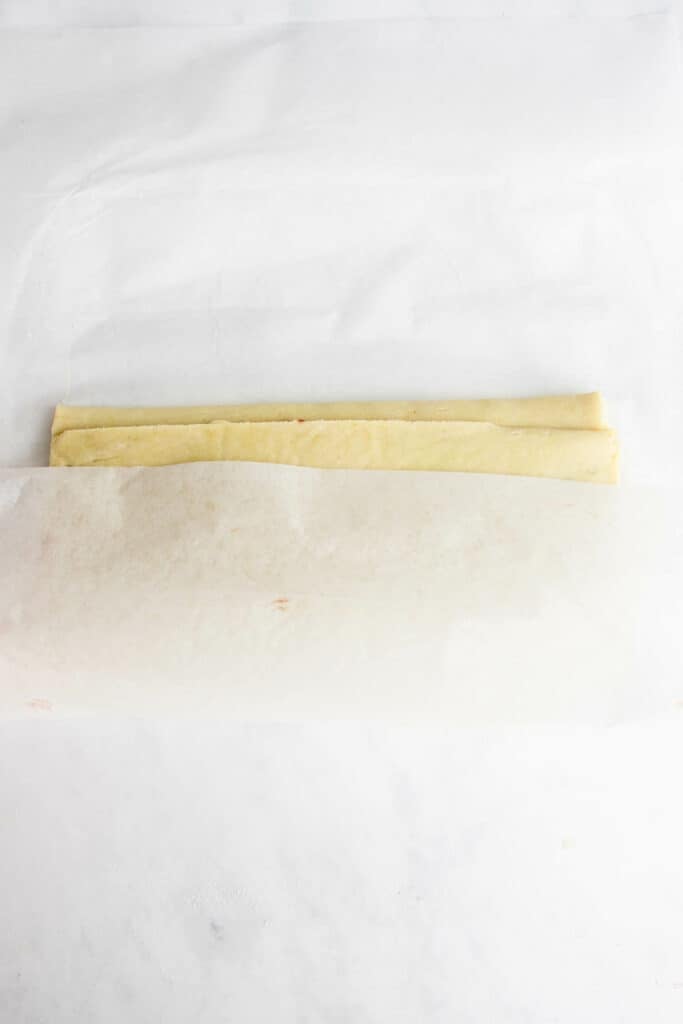 gluten free pizza dough folded into thirds with parchment paper 