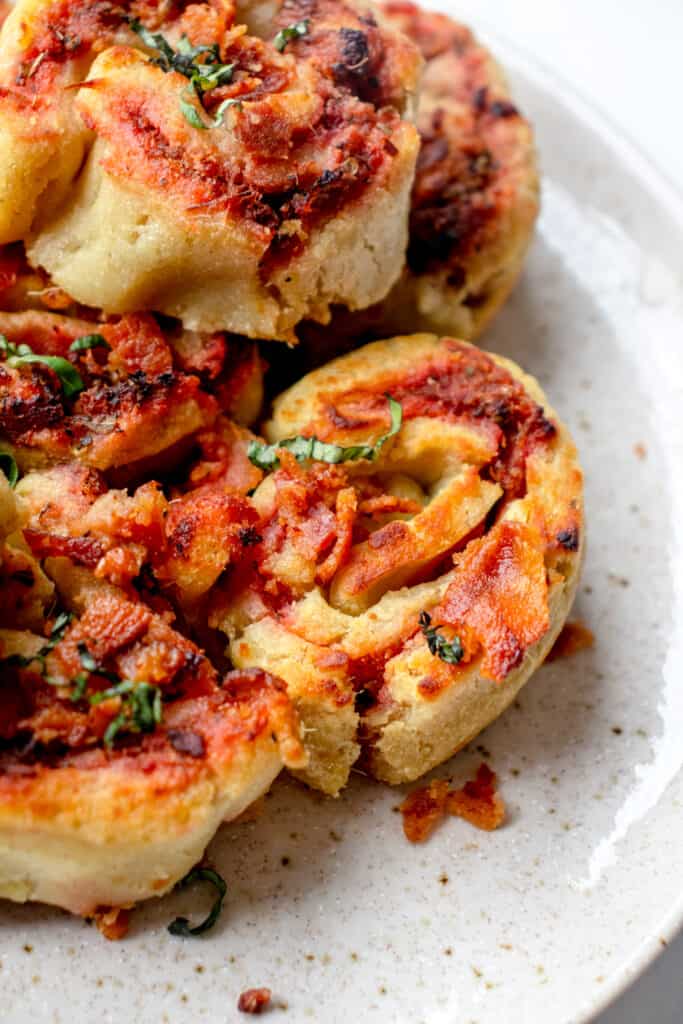 speckled brown plate with gluten free pizza rolls topped with crumbled bacon and chopped basil