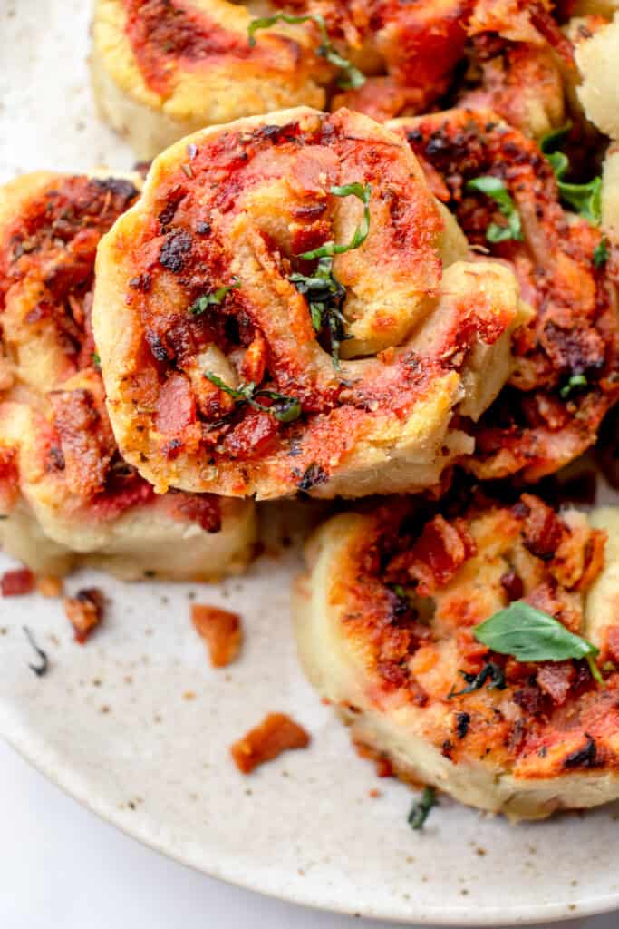 speckled brown plate with gluten free pizza rolls topped with crumbled bacon and chopped basil