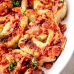 white oval casserole dish with gluten free pizza rolls topped with crumbled bacon and chopped basil