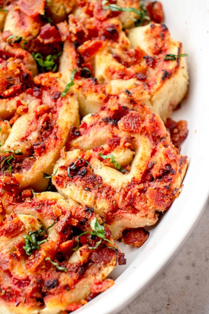 white oval casserole dish with gluten free pizza rolls topped with crumbled bacon and chopped basil