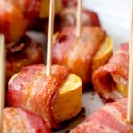 beige speckled plate with slices of sweet baked plantains wrapped in bacon. There are wooden toothpicks placed into some of the appetizers for serving
