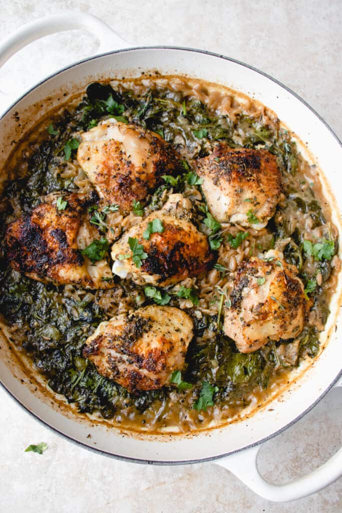 Cooked chicken thighs, cassava orzo and spinach garnished with fresh parsley, in a cast iron pan.