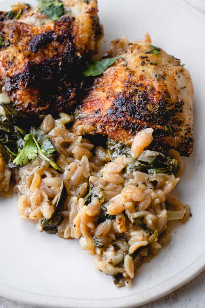 Two chicken thighs with cassava orzo and spinach on a white plate.