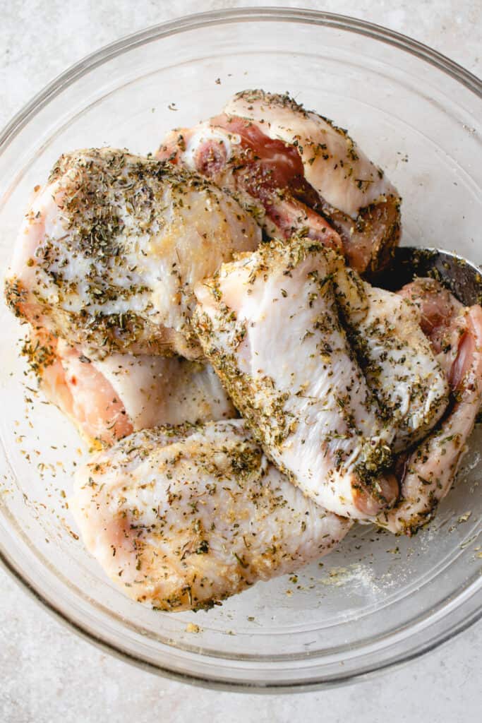 Seasoned chicken thighs in a large glass bowl.