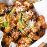 Paleo Crispy Orange Chicken garnished with green onions and toasted sesame seeds