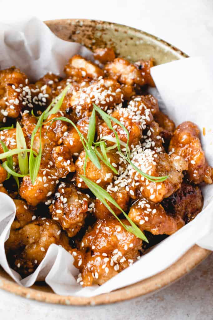 Paleo Crispy Orange Chicken garnished with green onions and toasted sesame seeds