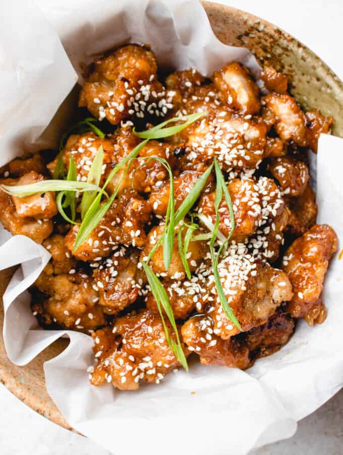 Bowl with crispy paleo orange chicken garnished with sesame seeds and green onions.