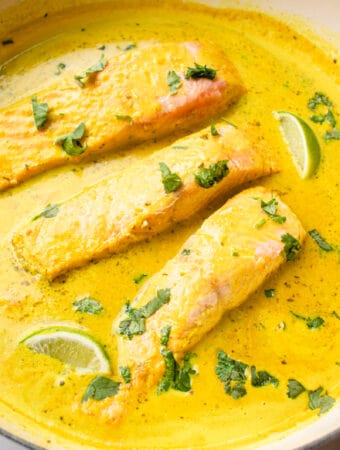 Salmon coconut curry dish in a pan, garnished with lime wedges and chopped cilantro.