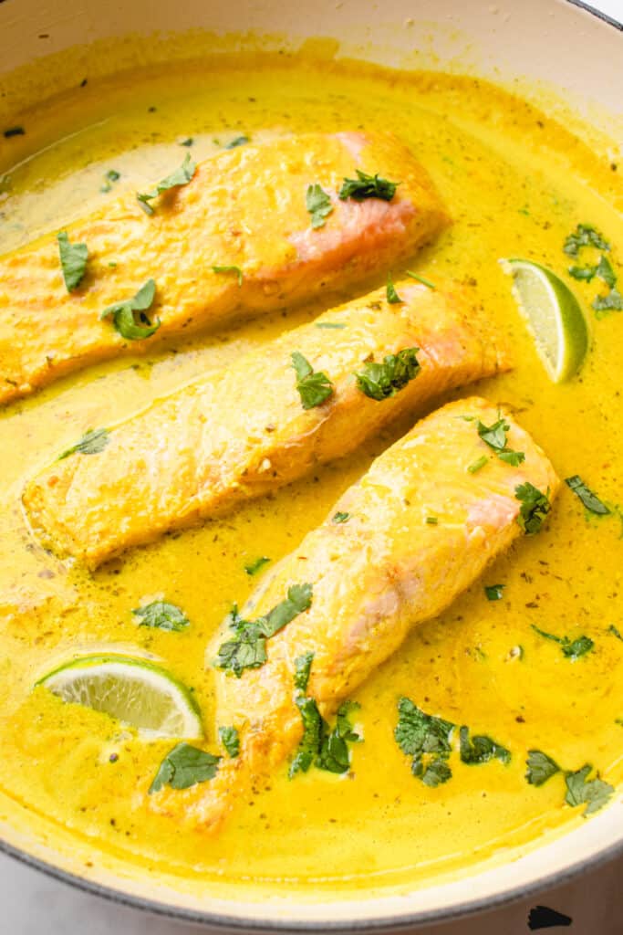 Salmon coconut curry dish in a pan, garnished with lime wedges and chopped cilantro.