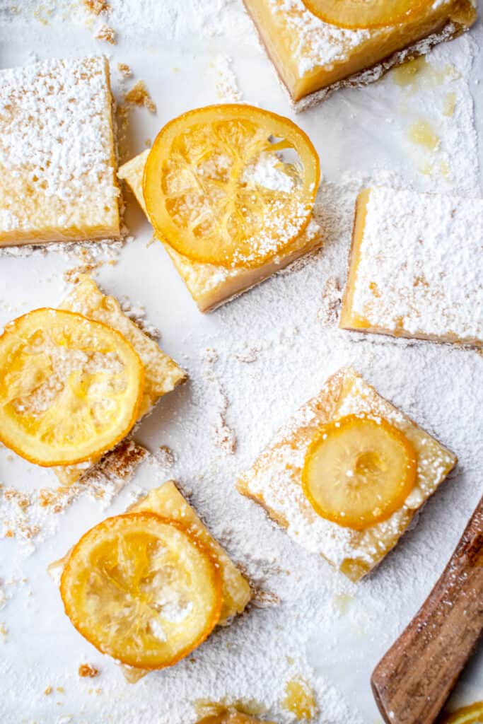Individual lemon bars dusted with arrowroot starch and candied lemon slices placed on top of them.