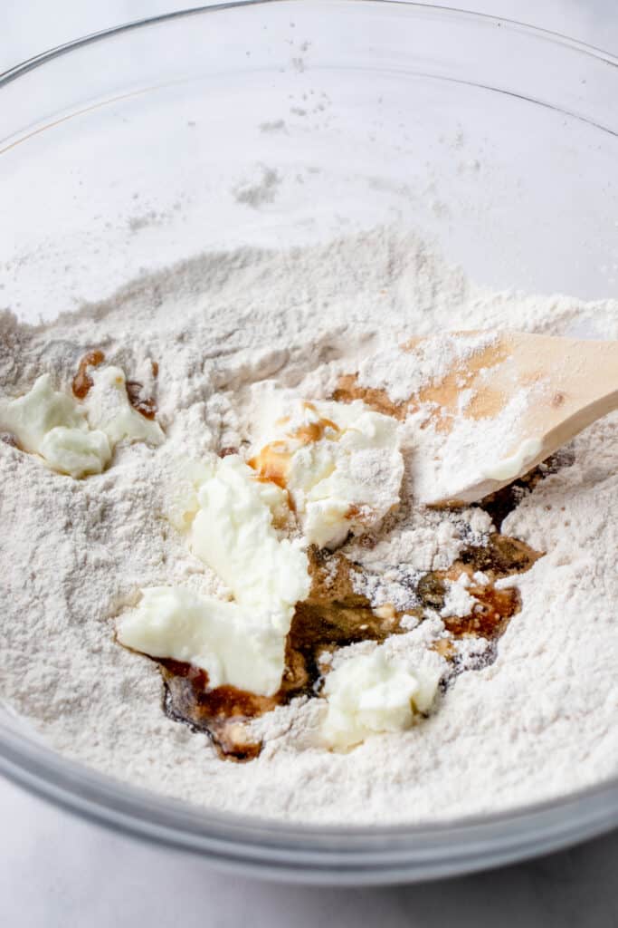 Glass bowl with the grain and gluten-free crust ingredients, and a wooden spoon about to mix the ingredients.