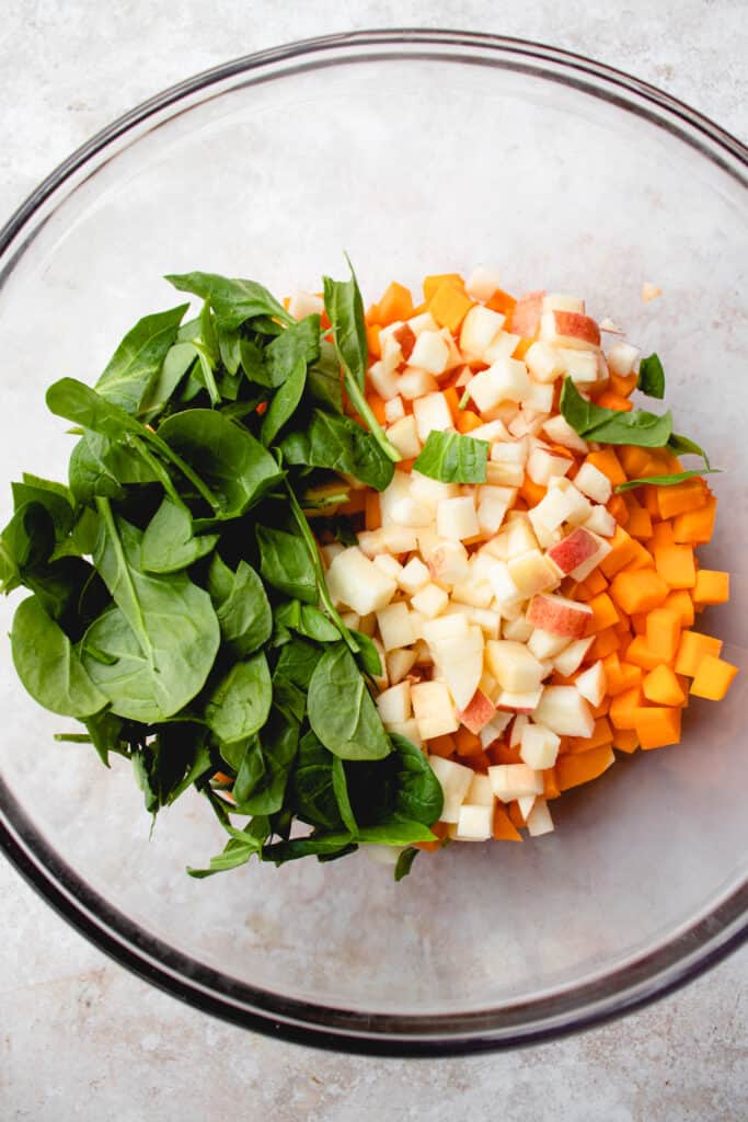 Spinach leaves, diced apple and cubed butternut squash in a glass bowl.