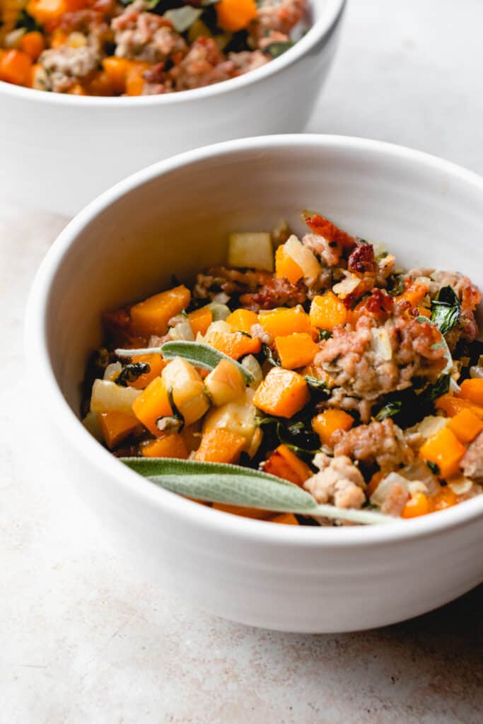 white bowls with butternut squash hash, garnished with fresh sage leaves.