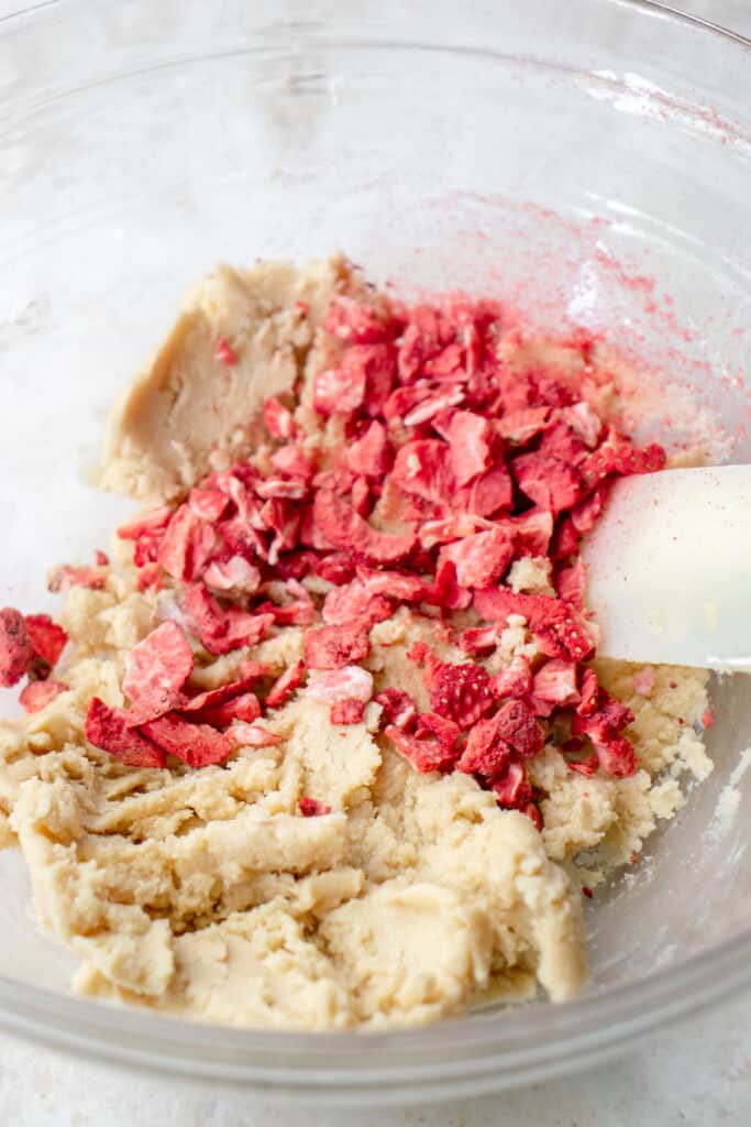 Freeze-dried strawberries added to sugar cookie dough in a glass bowl.