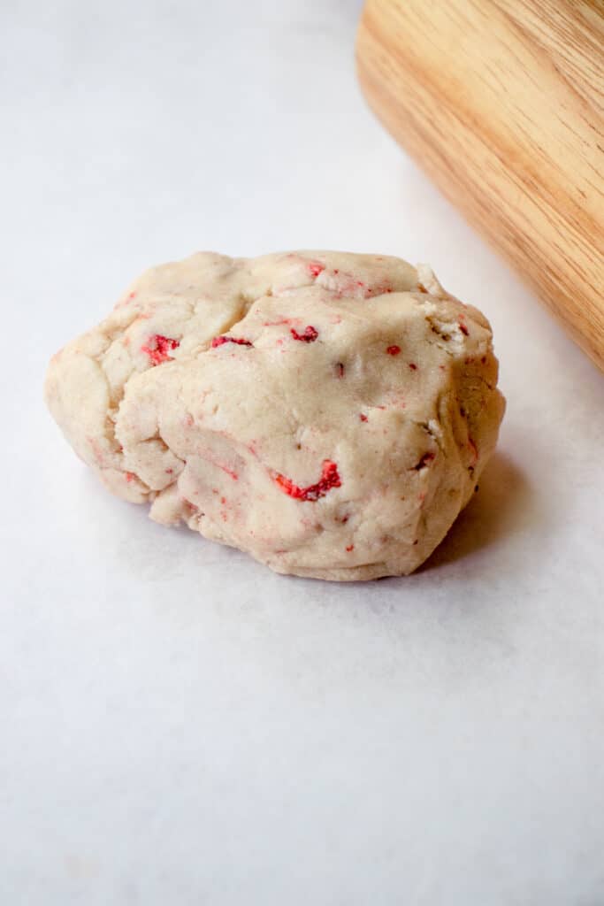 Strawberry sugar cookie dough on parchment paper next to a rolling pin.