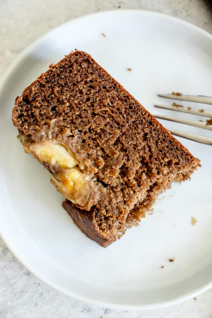 slice of banana bread broken into with a fork on a small white plate