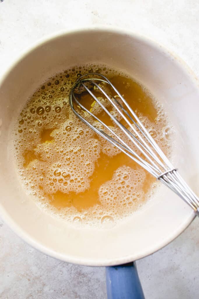 A saucepan with honey, water, sea salt and vanilla to make the honey mixture. A whisk is placed in the saucepan.