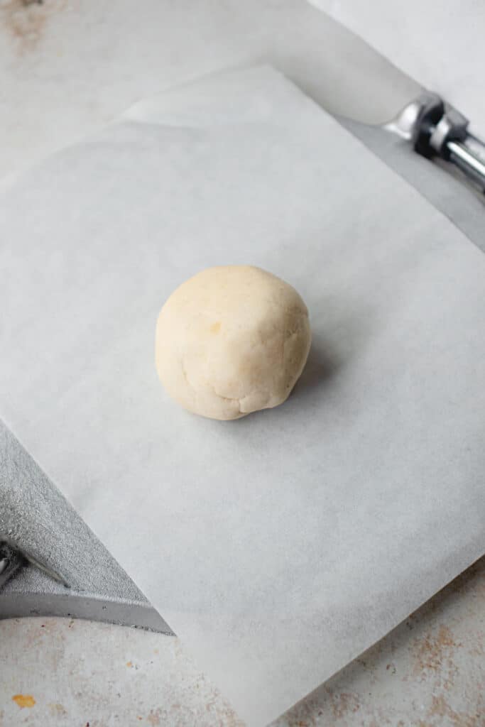 The bottom plate of a tortilla press lined with parchment paper, with a ball of dough in the middle.