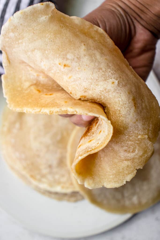 A brown hand holding a tortilla to show it is soft and bendable without cracking.