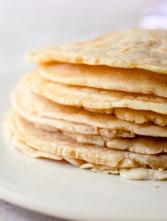 A close up of a stack of cassava flour tortillas on an off-white plate.