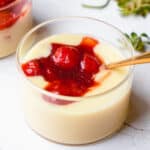 Close up of a short glass jar with lemon custard and strawberry compote with a gold spoon dipped in.