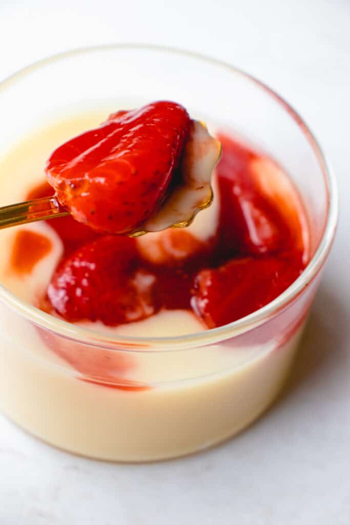 Close up shot of a spoon with strawberry compote and some lemon custard, held over a jar of the dessert.